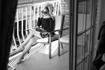 Glamour lady reading a magazine on balcony, hand on glasses
