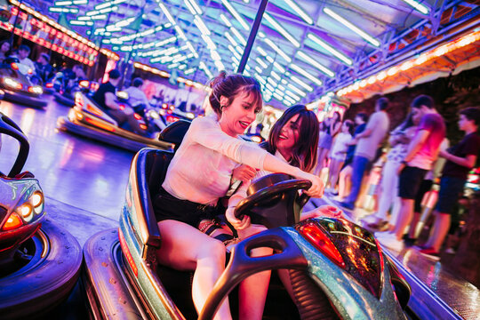 Two young women riding bumbper car on a funfair at night