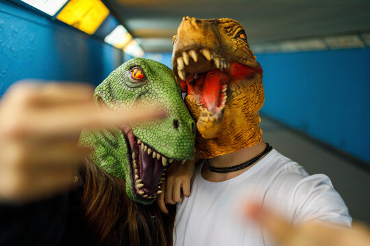 Male and female friends showing middle finger while wearing dinosaur mask in corridor