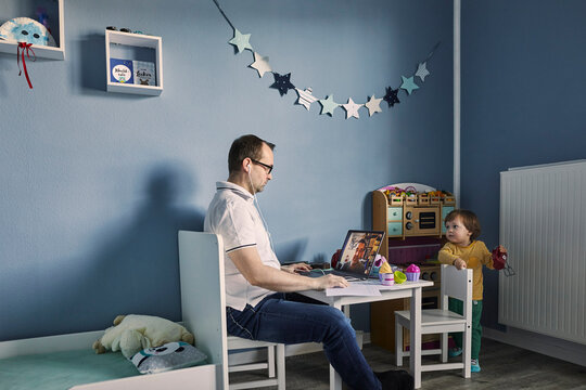 Man working and using laptop in children's room with simultaneous childcare