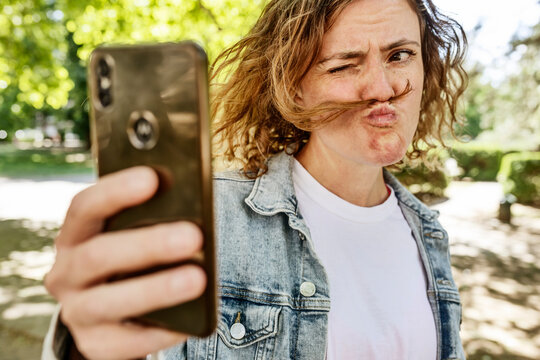Mid adult woman making face while taking selfie with mobile phone in park