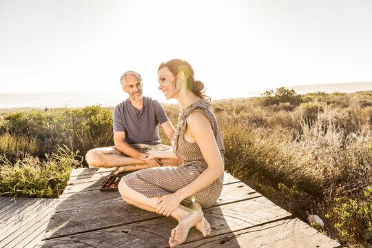 Couple sitting on boardwalk at the coast playing backgammon