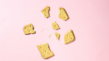 A broken cracker into small pieces on a pink background.
