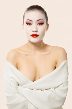 Young woman with opera make-up wrapped in blanket against white background