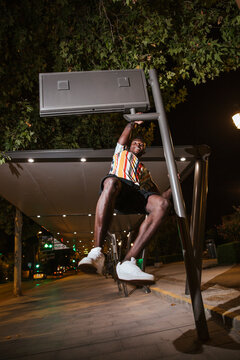 Playful young man hanging on a steet sign at night in the city