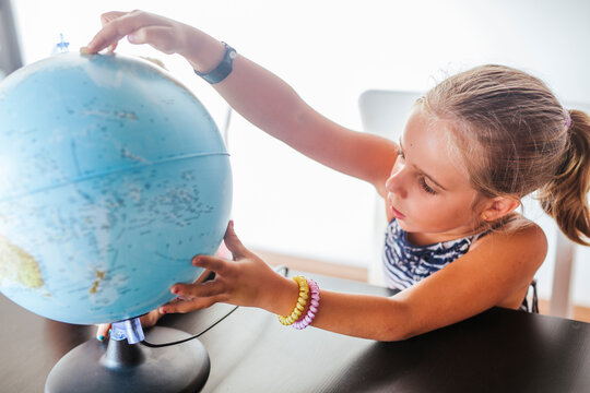 Curious schoolgirl looking at globe on desk - Powered by Adobe