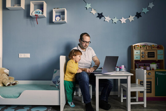 Man working and using laptop in children's room with simultaneous childcare