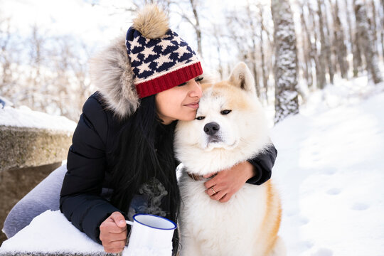 Woman with eyes closed embracing akita dog while holding coffee cup in winter