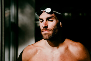 Shirtless male swimmer with eyes closed by window