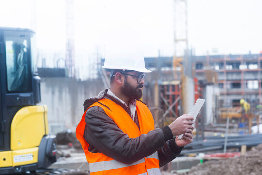 Construction engineer wearing hard hat and safety vest usimng tablet at construction site