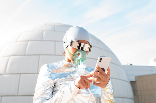 Woman in protective suit and oxygen mask using mobile phone while standing against igloo