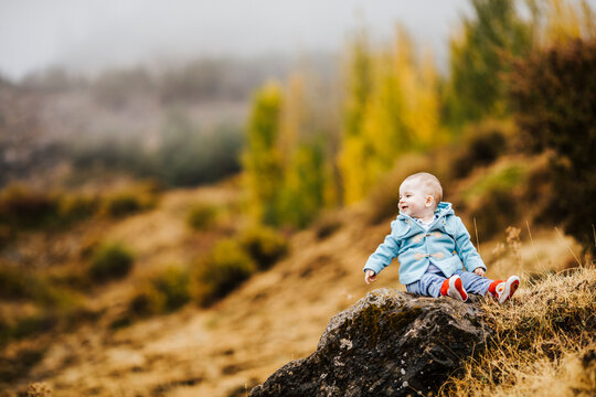 Happy baby boy siiting on rock in autumnal nature