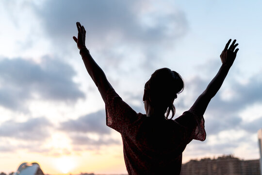 Woman standing arms raised watching sunset