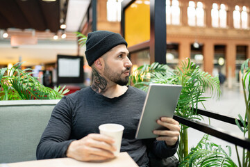 Hipster man with coffee cup holding digital tablet at table in cafe