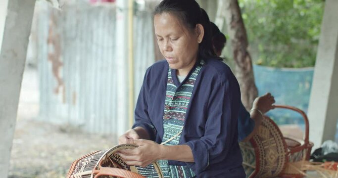 A smiling Thai female farmer weave baskets in traditional Thai art patterns to sell as extra income in countryside of Thailand.