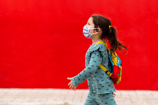 Girl walking with backpack and mask along red wall