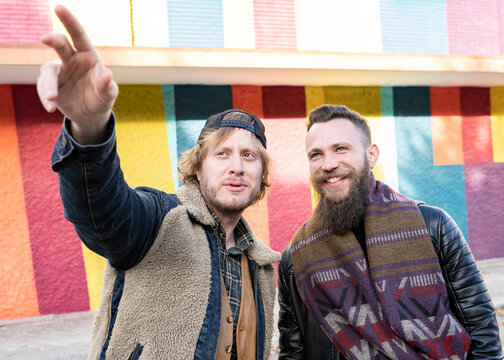 Man pointing while standing with boyfriend against multi colored wall in city