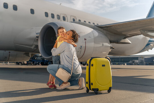 Happy mom hugging her daughter before flying on a big white plane. Trip concept