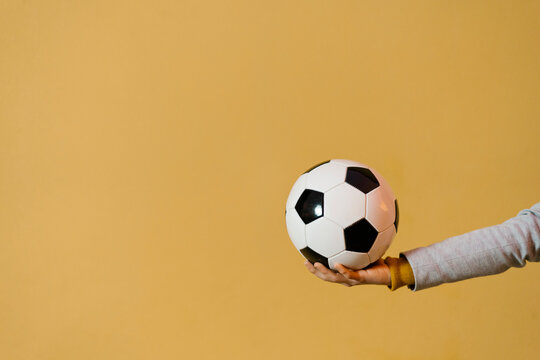 Fototapeta Young man holding soccer ball against yellow wall