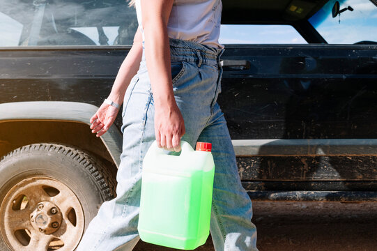 Midsection of woman carrying coolant gallon container while walking by 4x4 vehicle on sunny day