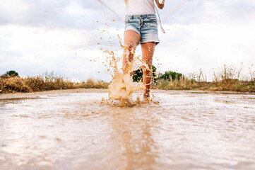 Girl splashing water in puddle against sky