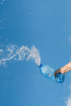 Hand of woman splashing water from bottle against blue sky