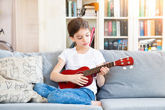 Portrait of girl sitting on couch at home playing ukulele