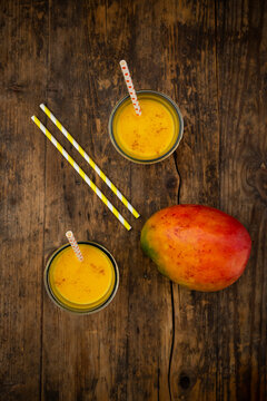 Mango and two glasses of Mango Lassi with curcuma and straws on wood