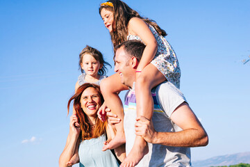 Fototapeta na wymiar Cheerful parents carrying daughters on shoulders against clear sky during sunny day