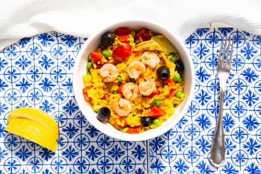 Paella with rice, bell pepper, tomato, artichoke, pea, black olive, curcuma and shrimps