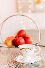 Red ripe apples lie in a glass vase on the table next to cups of tea