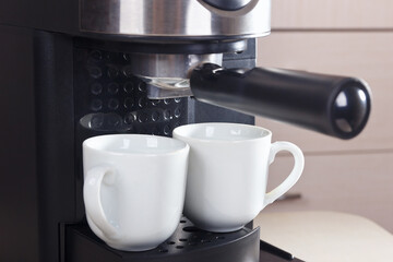 Two white cups for coffee under carob coffee maker.
