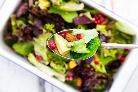 Detox salad bowl with avocado, pomegranate seeds, roasted soybeans, sunflower seeds and nuts, on spoon