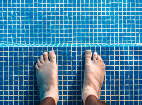 Feet of man standing ankle deep in swimming pool