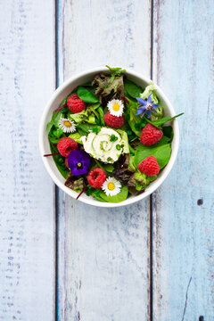 Bowl of leaf salad with raspberries and cream cheese garnished with edible flowers