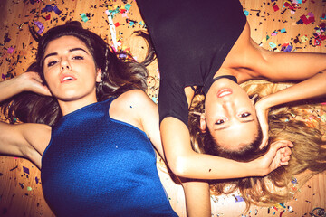 Female friends lying on floor covered with confetti in party
