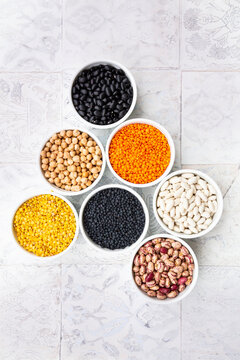 Various legumes in bowls: chickpeas, cannellini beans, quail beans, black beans, yellow lentils, red lentils, black lentils