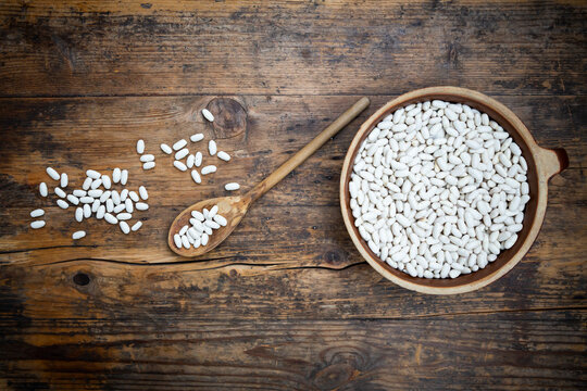 Overhead view of bowl of white cannellini beans on wooden table