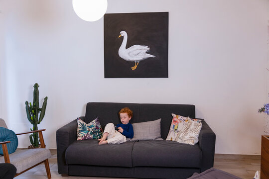 Cute boy playing with joystick while relaxing on sofa in living room at home