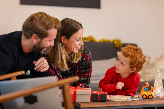 Smiling Parents And Son Looking At Each Other In Living Room During Christmas