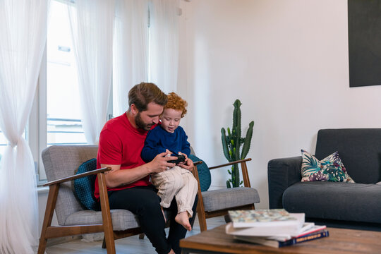 Father with cute son holding joystick while playing video game in living room at home