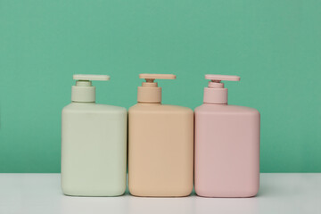 Three bottles for cosmetics with dispensers of different colors for soap, shower gel, shampoo, hair conditioner, on a green background