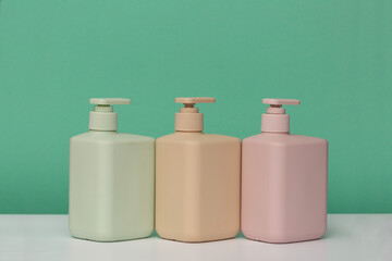 Three bottles for cosmetics with dispensers of different colors for soap, shower gel, shampoo, hair conditioner, on a green background