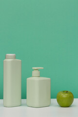 two light green jars for cosmetic soap, shower gel, shampoo, hair conditioner and a green apple on a green background