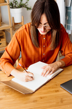 Female freelancer working at home sitting at desk taking notes