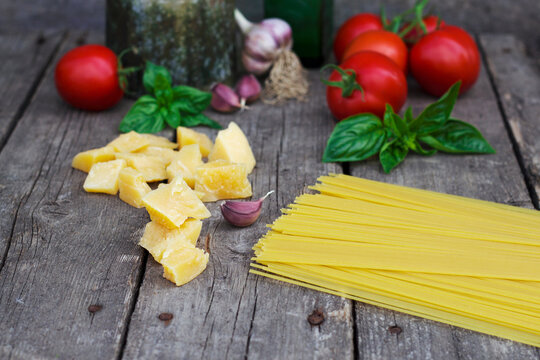Pasta with tomatoes, basil, parmesan cheese and garlic cloves on the old wooden table. Cooking ingredients for spagetty with souse recipe. Italian cuisine for dinner.