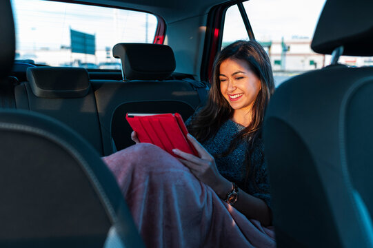 Smiling young woman using digital tablet while sitting on backseat of car with blanket