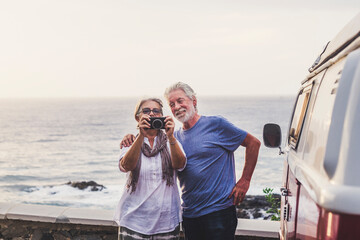 Senior couple traveling in a vintage van, taking pictures at the sea