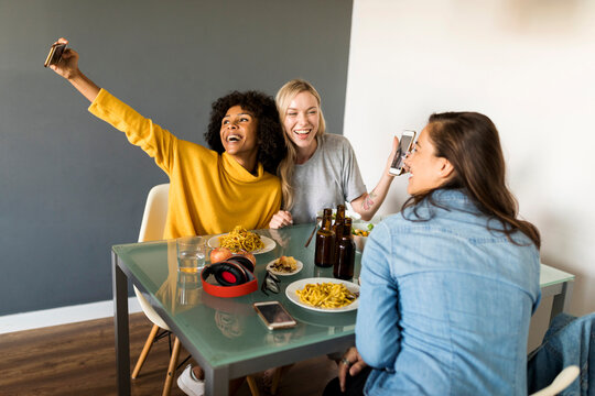 Happy girlfriends sitting at dining table taking a selfie
