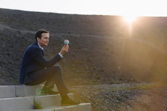 Mature businessman holding a miniature globe on a disused mine tip